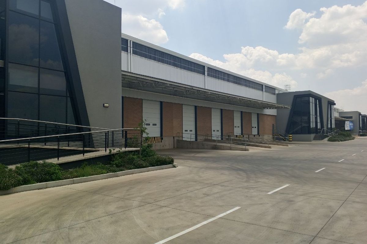 Modern industrial warehouse facility featuring multiple loading docks with roller shutter doors, concrete yard space, and contemporary glass and metal architectural elements.