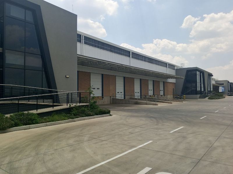 Modern industrial warehouse facility featuring multiple loading docks with roller shutter doors, concrete yard space, and contemporary glass and metal architectural elements.