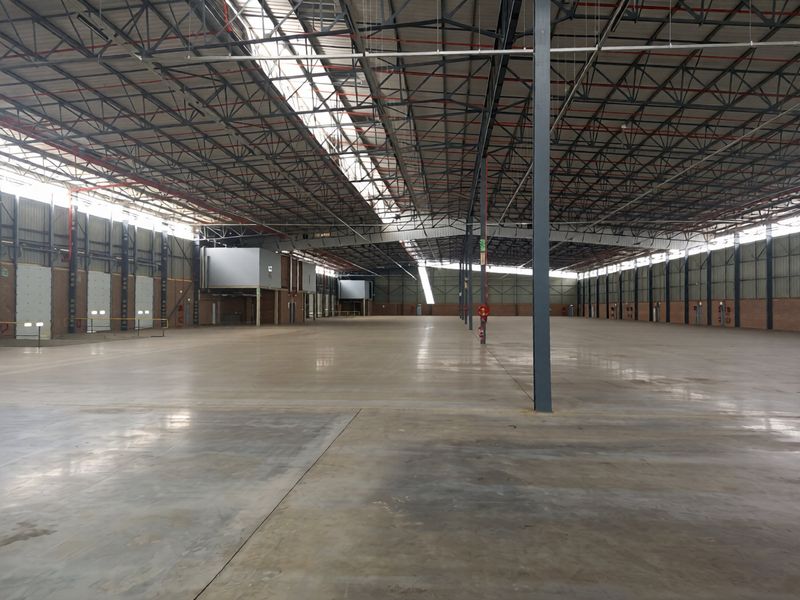 Expansive industrial warehouse space featuring high ceilings with exposed steel trusses, polished concrete flooring, and integrated fire sprinkler systems.