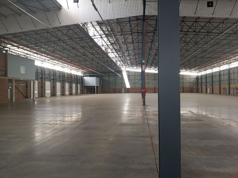 Expansive industrial warehouse space featuring high-clearance steel truss roofing, polished concrete flooring, and abundant natural light through integrated skylights.