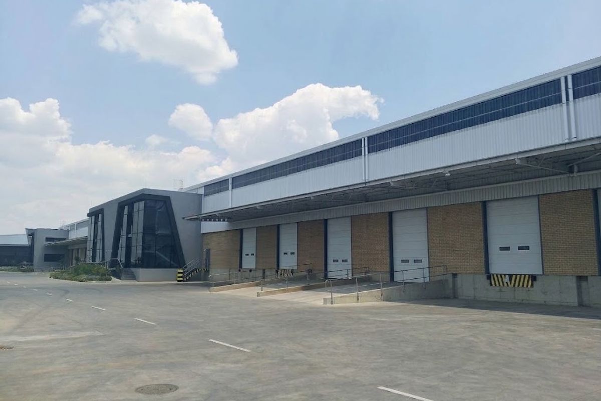Industrial warehouse facility featuring multiple loading docks with roller shutter doors, a large concrete yard, and a modern glass-fronted office entrance.