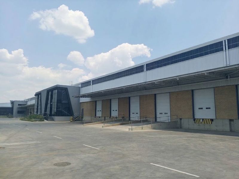 Industrial warehouse facility featuring multiple loading docks with roller shutter doors, a large concrete yard, and a modern glass-fronted office entrance.