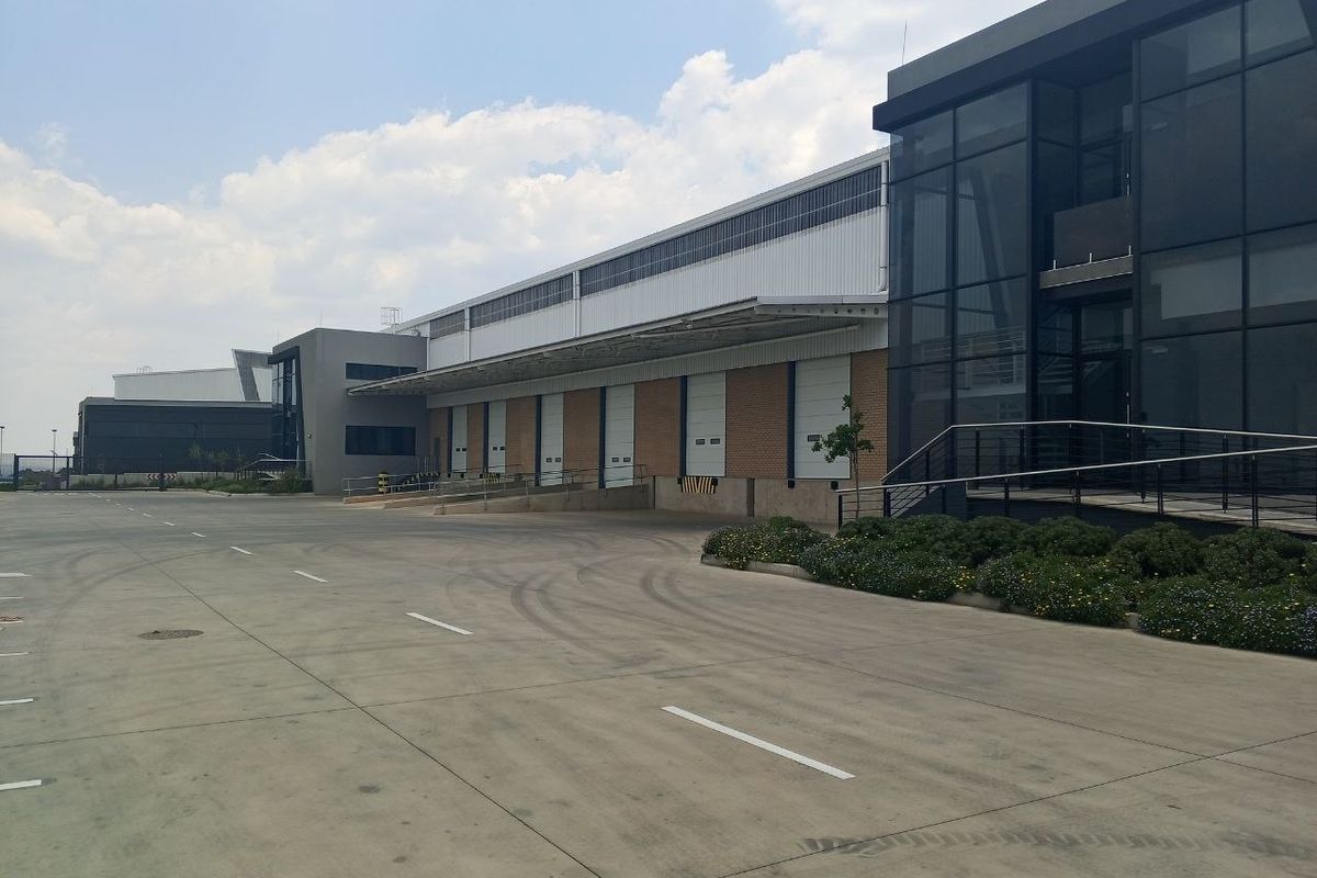 Modern industrial warehouse facility featuring multiple loading bays with roller shutter doors, a large concrete yard, and contemporary glass-fronted office components.