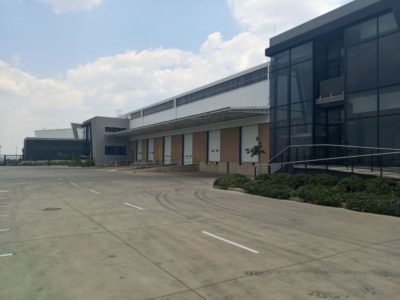 Modern industrial warehouse facility featuring multiple loading bays with roller shutter doors, a large concrete yard, and contemporary glass-fronted office components.