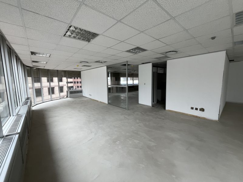 An expansive, vacant office space featuring large floor-to-ceiling windows, a suspended ceiling with recessed lighting, and a modern glass partition wall.