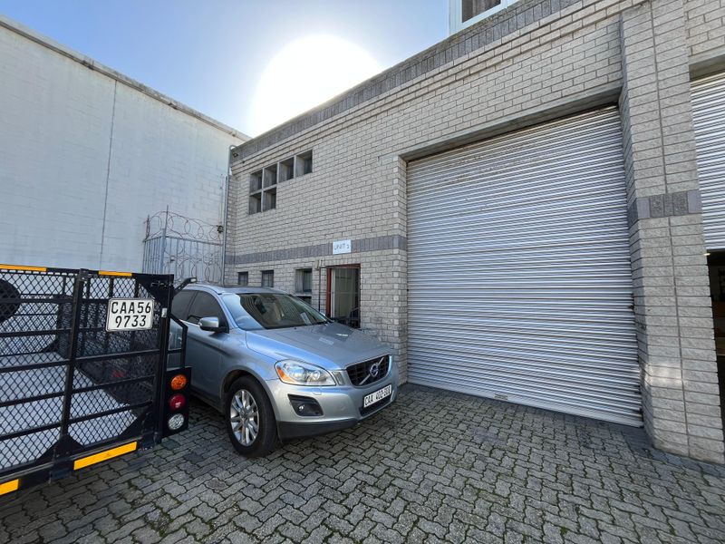 Industrial unit exterior featuring a large roller shutter door, brick facade, and paved driveway access.
