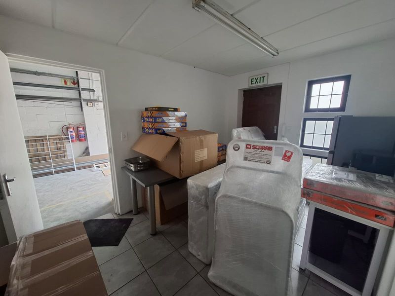 A functional utility or storage space featuring tiled flooring, fluorescent lighting, and direct access to an adjacent industrial area.