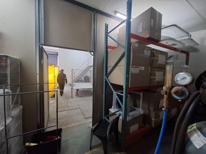 Industrial utility space featuring heavy-duty metal shelving units and concrete flooring, providing functional storage within an active workshop environment.