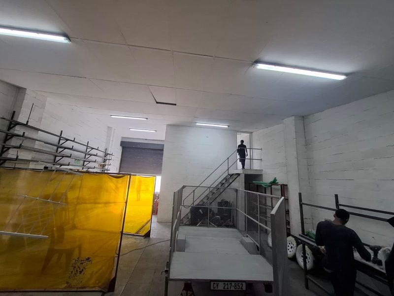 Industrial utility space featuring a mezzanine level with metal staircase, roller shutter door access, and overhead fluorescent lighting.