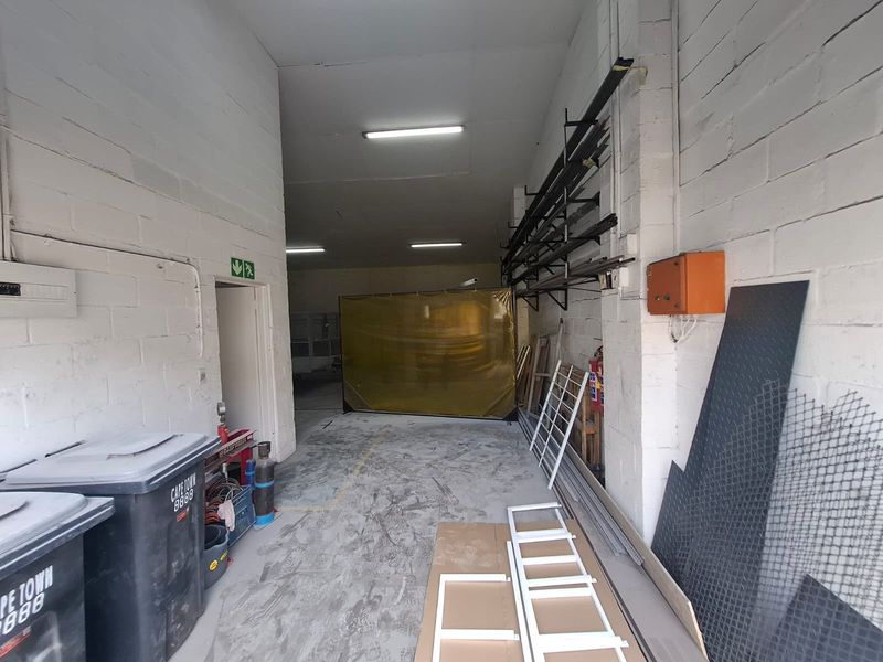 Industrial utility space featuring exposed concrete block walls, fluorescent lighting, and wall-mounted storage racking, suitable for workshop or storage use.