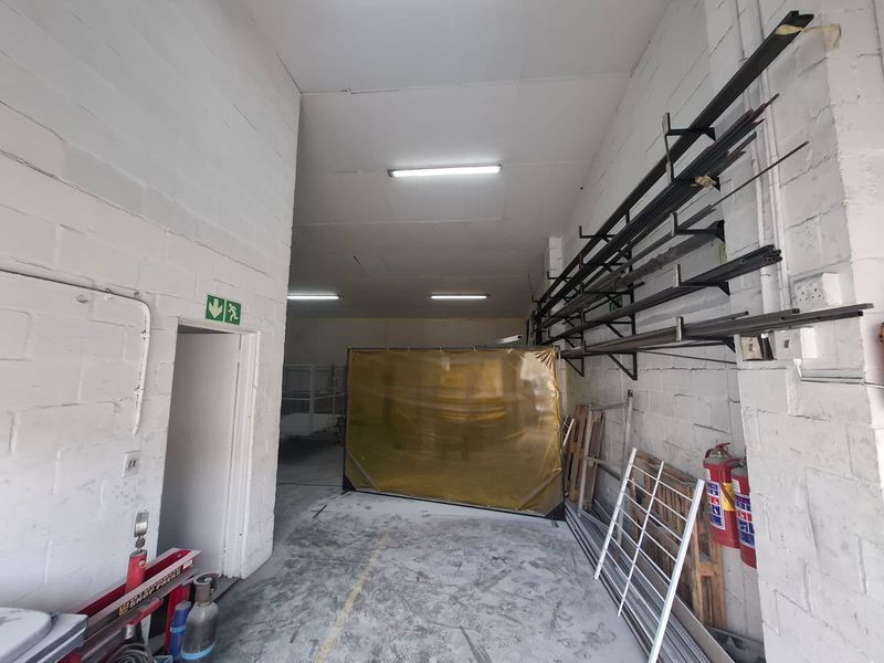 Industrial utility space featuring exposed brick walls, fluorescent lighting, and wall-mounted metal storage racks, suitable for workshop or storage use.