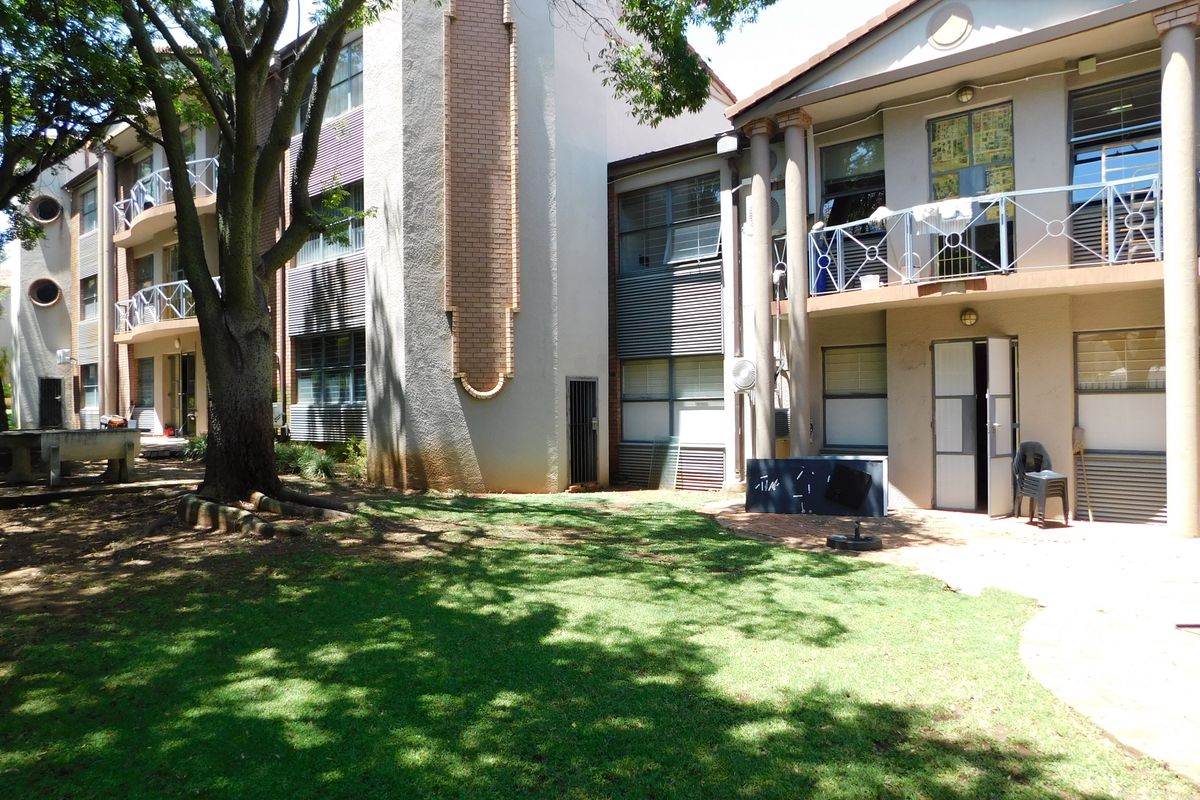 Exterior view of a multi-story office building featuring balconies, large windows, and a landscaped garden area with mature trees.
