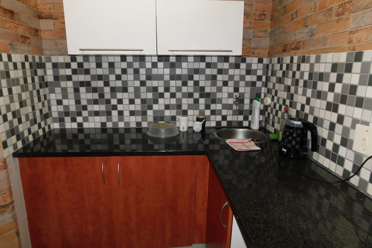 Compact kitchenette featuring dark granite countertops, wooden cabinetry, white overhead cupboards, and a mosaic tile backsplash.
