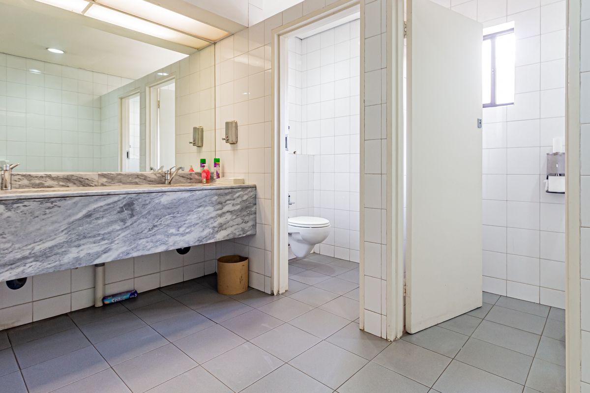 A functional office restroom featuring a marble-topped vanity with a large mirror, tiled walls, and separate toilet cubicles.
