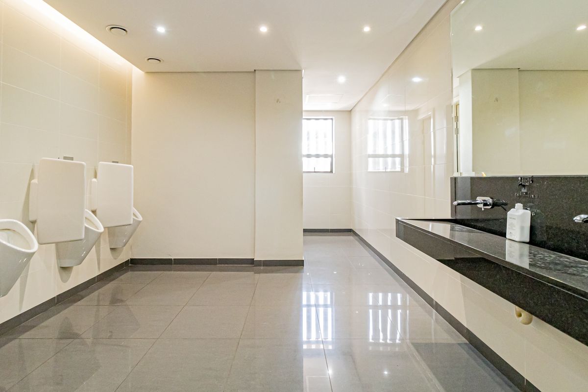 Modern commercial restroom featuring wall-mounted urinals, a sleek granite vanity with integrated sinks, and polished floor tiles.