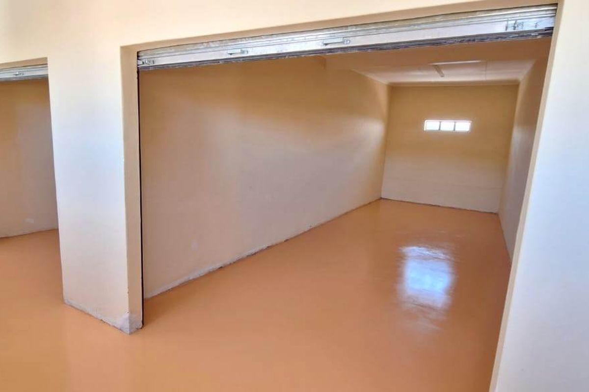 A clean, empty retail or storage space featuring smooth, polished flooring and multiple access points with roller shutter doors.
