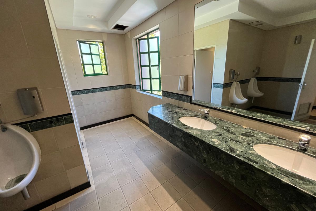 A commercial office restroom featuring a green marble vanity with dual basins, wall-mounted urinals, and tiled flooring.