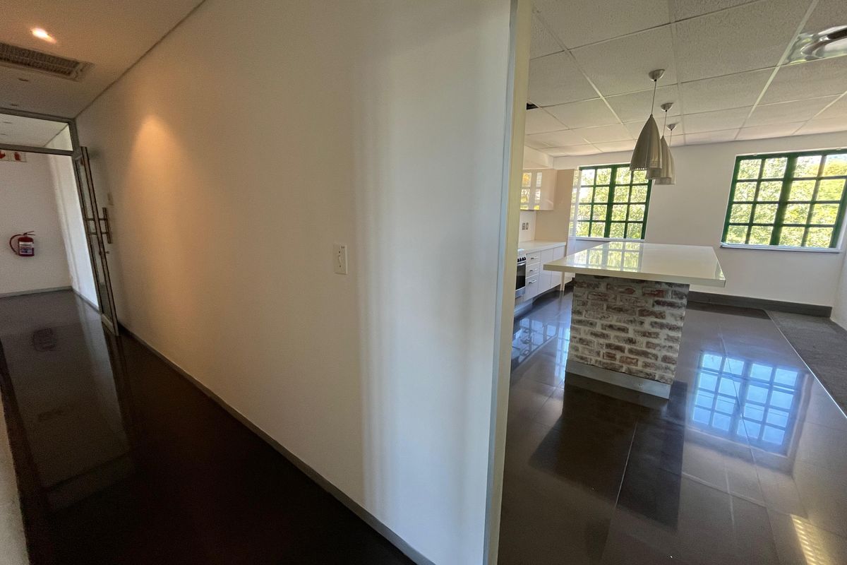 A bright office kitchen area featuring a central island with a brick base, tiled flooring, and large windows providing natural light.