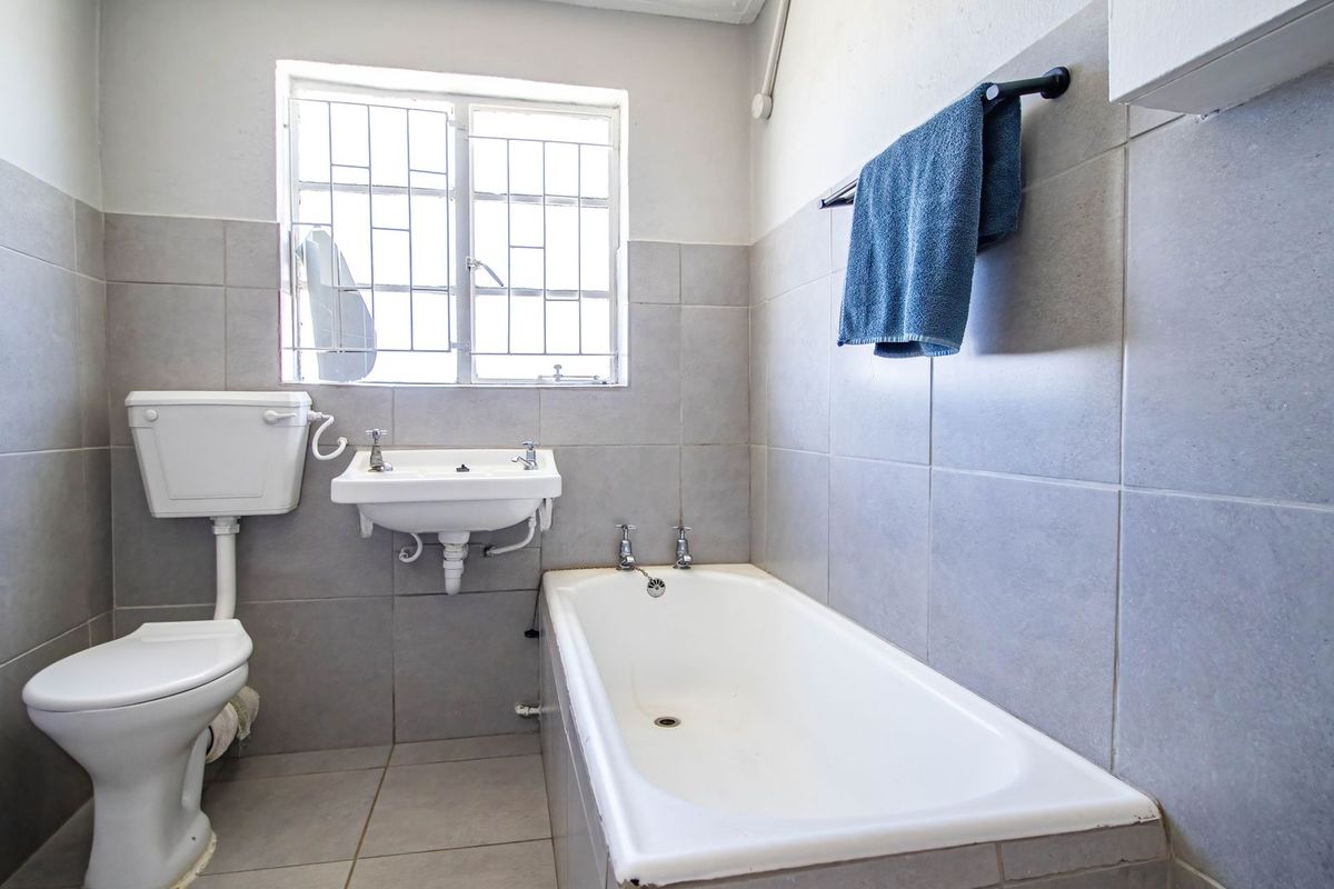 A functional bathroom featuring a standard bathtub, wall-mounted basin, and toilet with neutral grey wall and floor tiling.