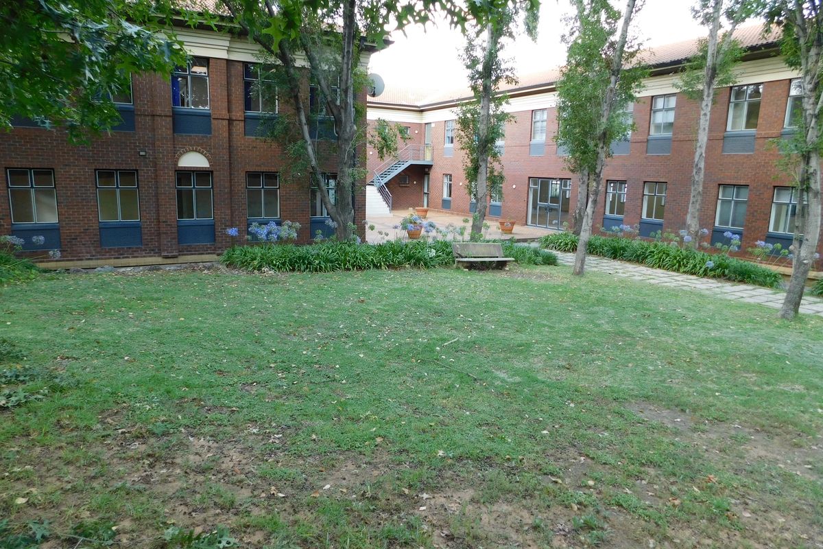 A view of the office building exterior featuring a central courtyard with a lawn, paved pathways, and mature trees.