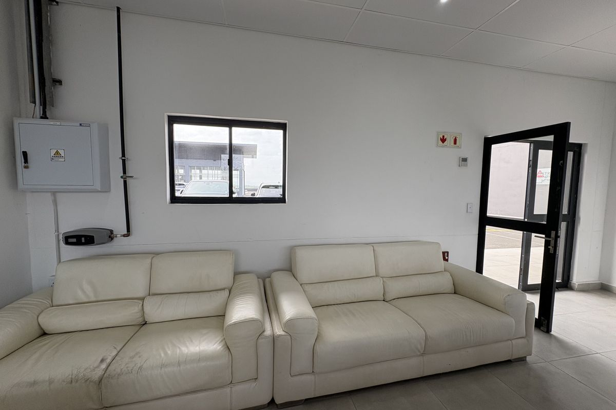 A functional retail office or waiting area featuring tiled flooring, a suspended ceiling, and a secure glass-panelled entrance door.