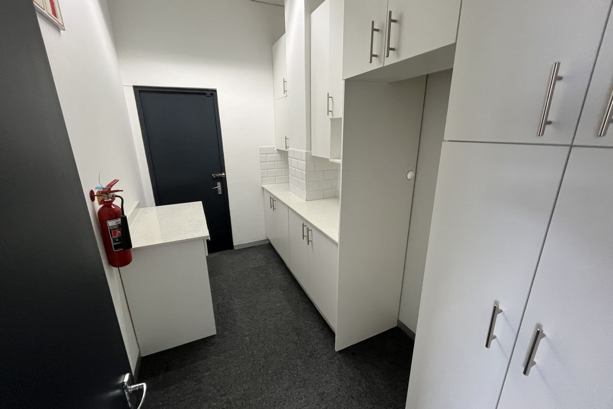 A clean office kitchenette area featuring white cabinetry, stone-look countertops, subway tile backsplash, and dark grey carpeting.