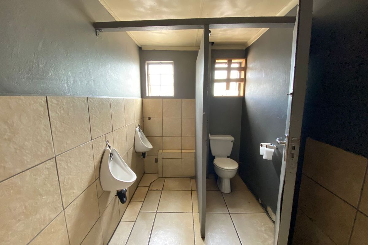 Functional industrial restroom facility featuring wall-mounted urinals and a private toilet cubicle with tiled flooring and walls.