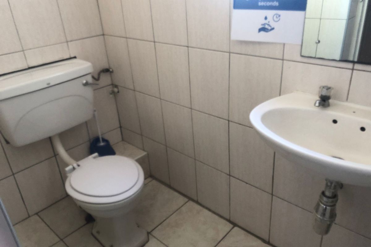 A functional office restroom featuring a standard white toilet, wall-mounted basin, and full-height wall tiling.
