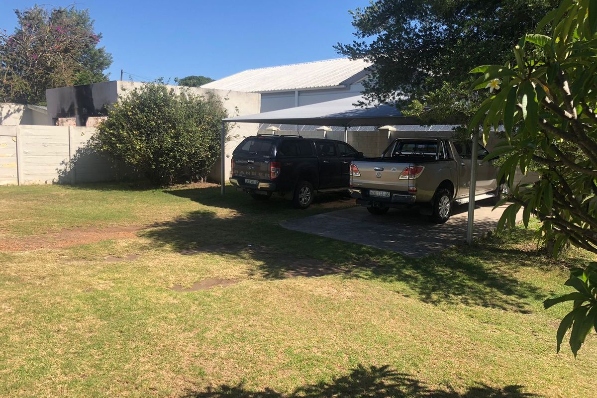 Outdoor area featuring a paved parking space with a shade cloth carport structure and a surrounding garden.