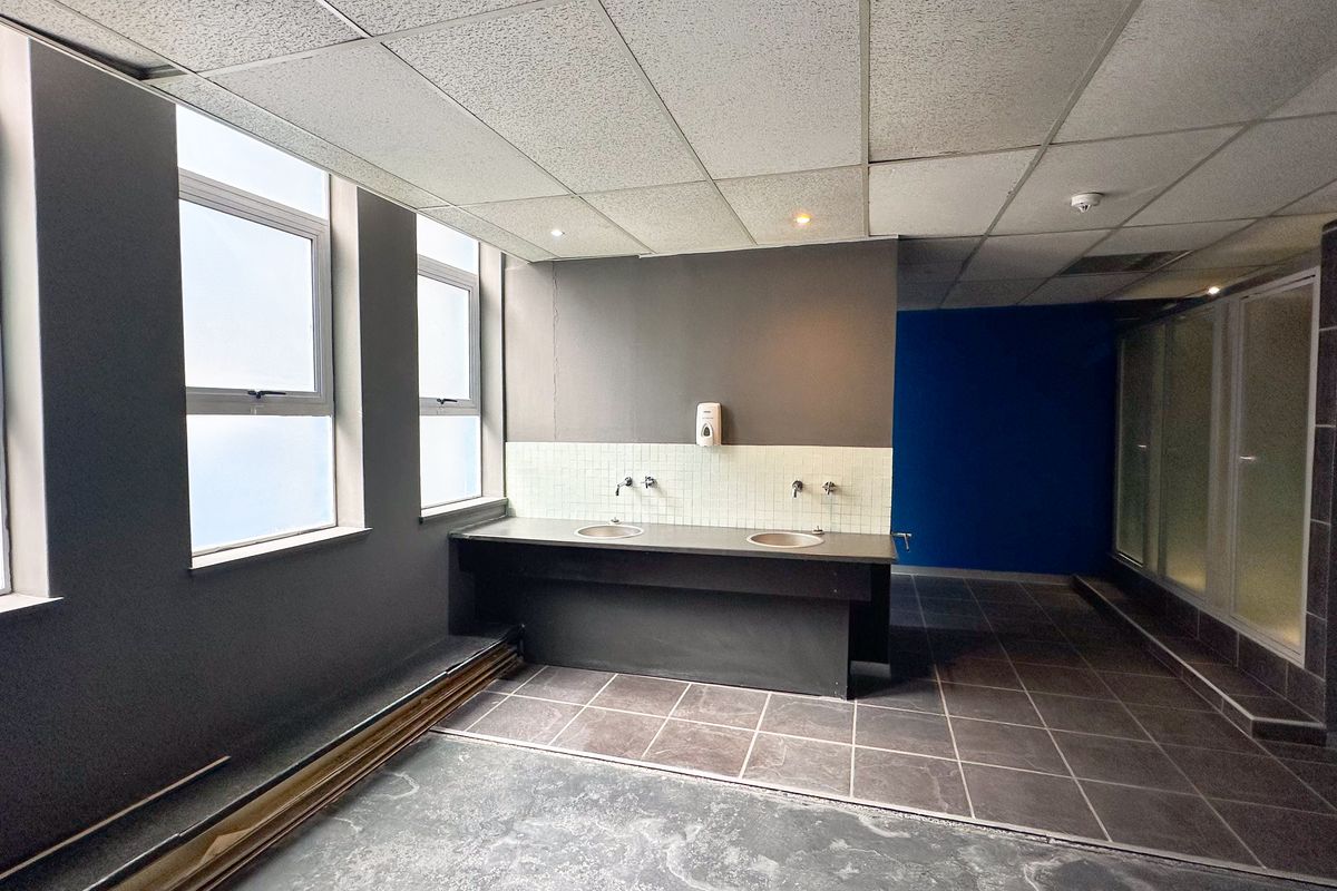 Office washroom area featuring dual integrated sinks, tiled backsplash, and adjacent shower cubicle with large windows providing natural light.