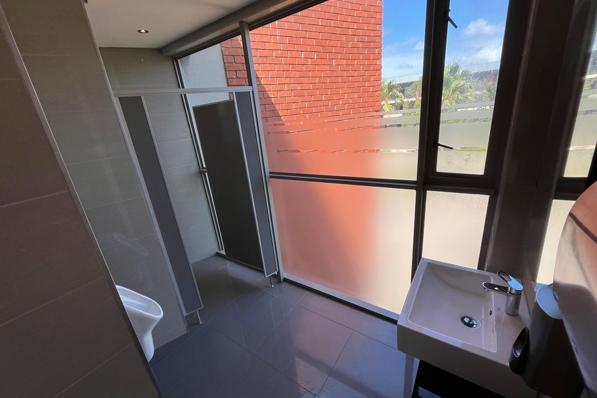 Modern office restroom featuring a wall-mounted basin, floor-to-ceiling windows with privacy film, and tiled flooring.
