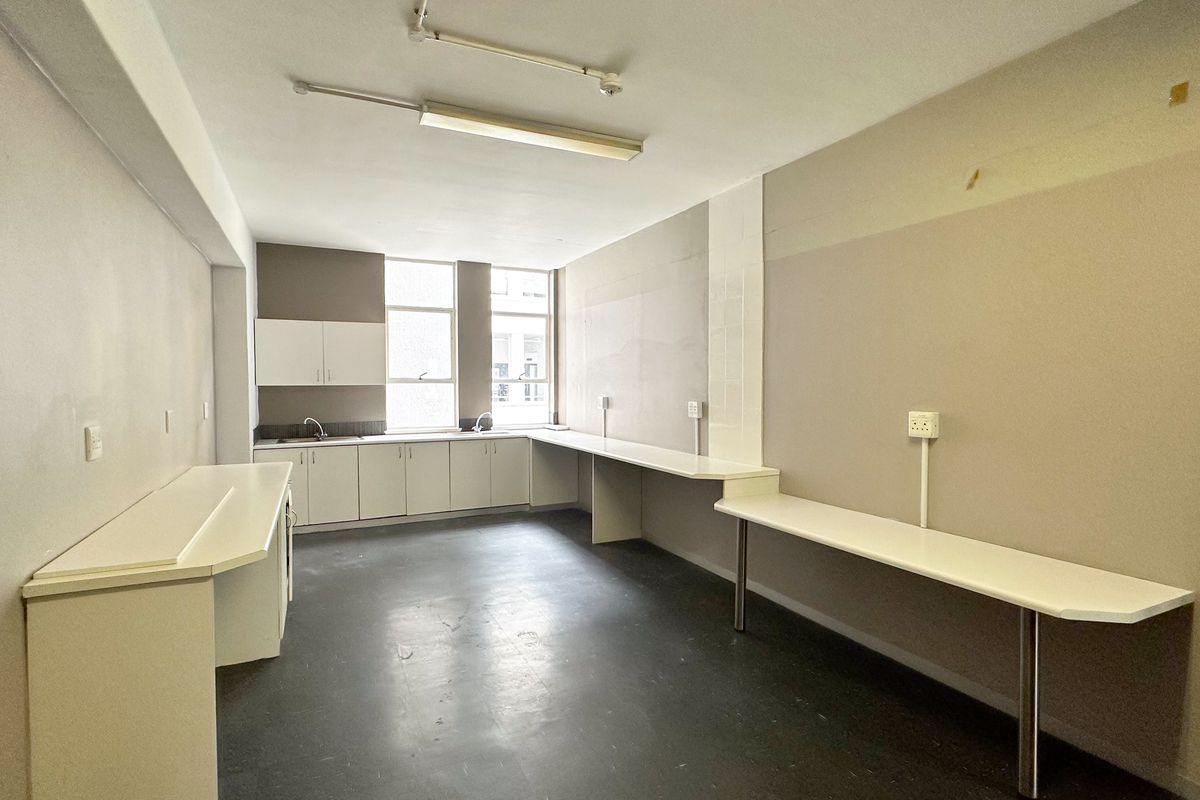 A functional office kitchenette featuring built-in cabinetry, laminate countertops, and a stainless steel sink, providing a practical workspace for staff.
