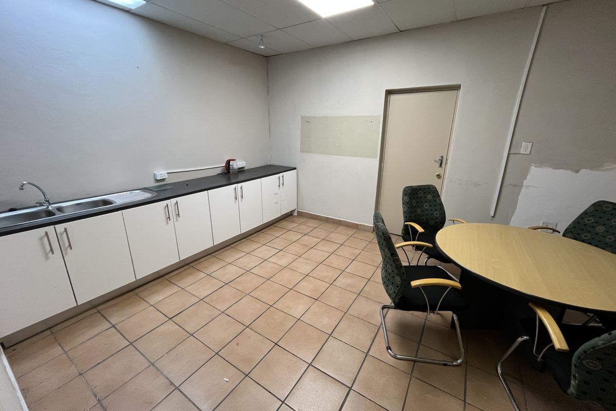 A functional office kitchenette area featuring built-in cabinetry, a stainless steel sink, tiled flooring, and recessed ceiling lighting.