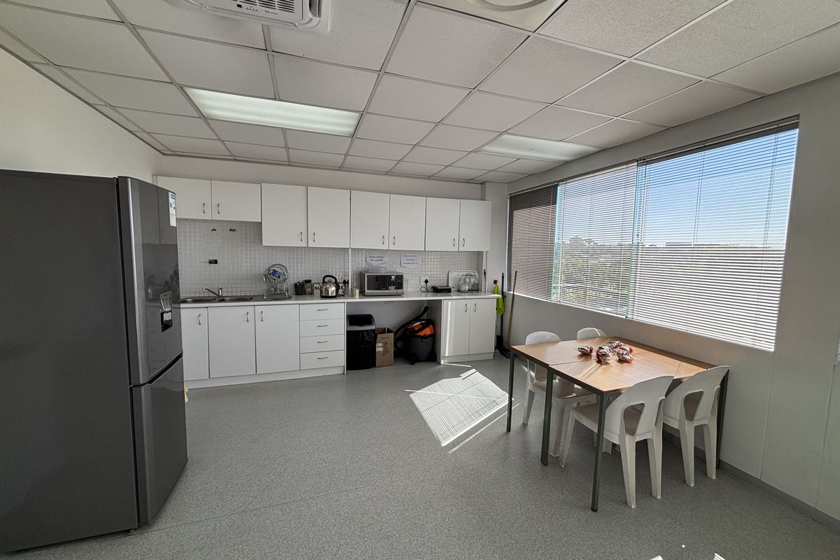 A functional office kitchenette featuring white cabinetry, tiled backsplash, integrated sink, and a suspended ceiling with recessed lighting.