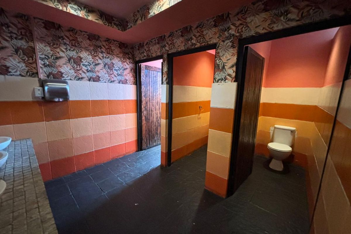 A communal office restroom featuring multiple stalls, tiled flooring, and a vanity area with integrated sinks.