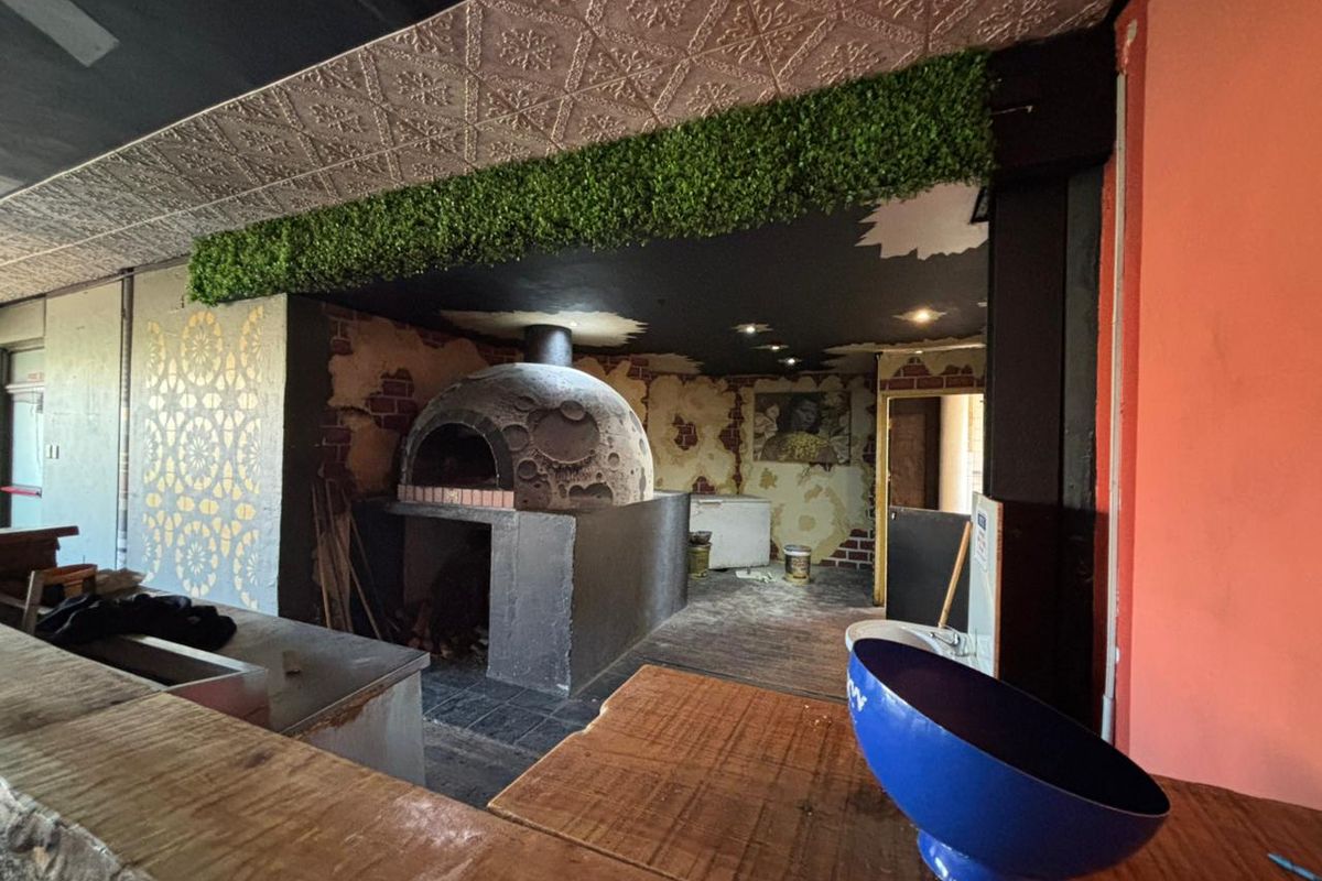 A commercial kitchen area featuring a built-in stone pizza oven, decorative ceiling tiles, and a service counter in an office or restaurant setting.