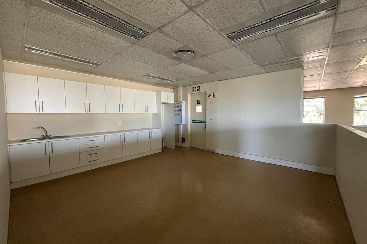 A functional office kitchenette area featuring built-in white cabinetry, a stainless steel sink, and a suspended acoustic ceiling with integrated lighting.