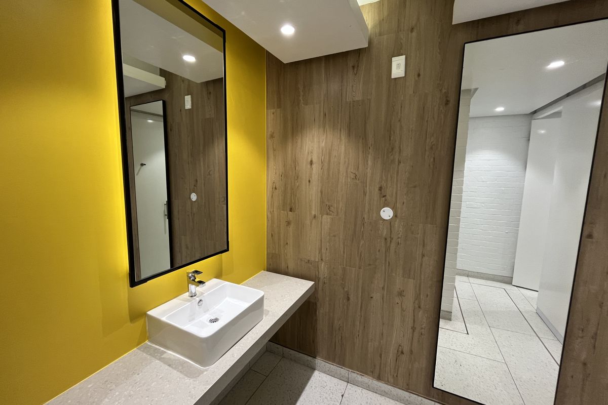Modern office restroom featuring a contemporary vessel sink, stone-look vanity countertop, wood-effect wall paneling, and large wall-mounted mirrors.