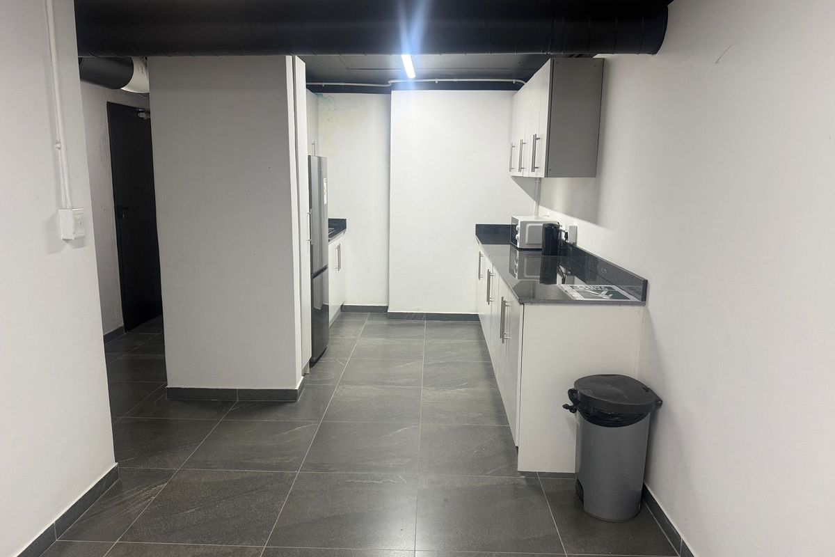 A functional kitchenette featuring white cabinetry, dark granite countertops, and dark floor tiling with an industrial-style exposed ceiling.