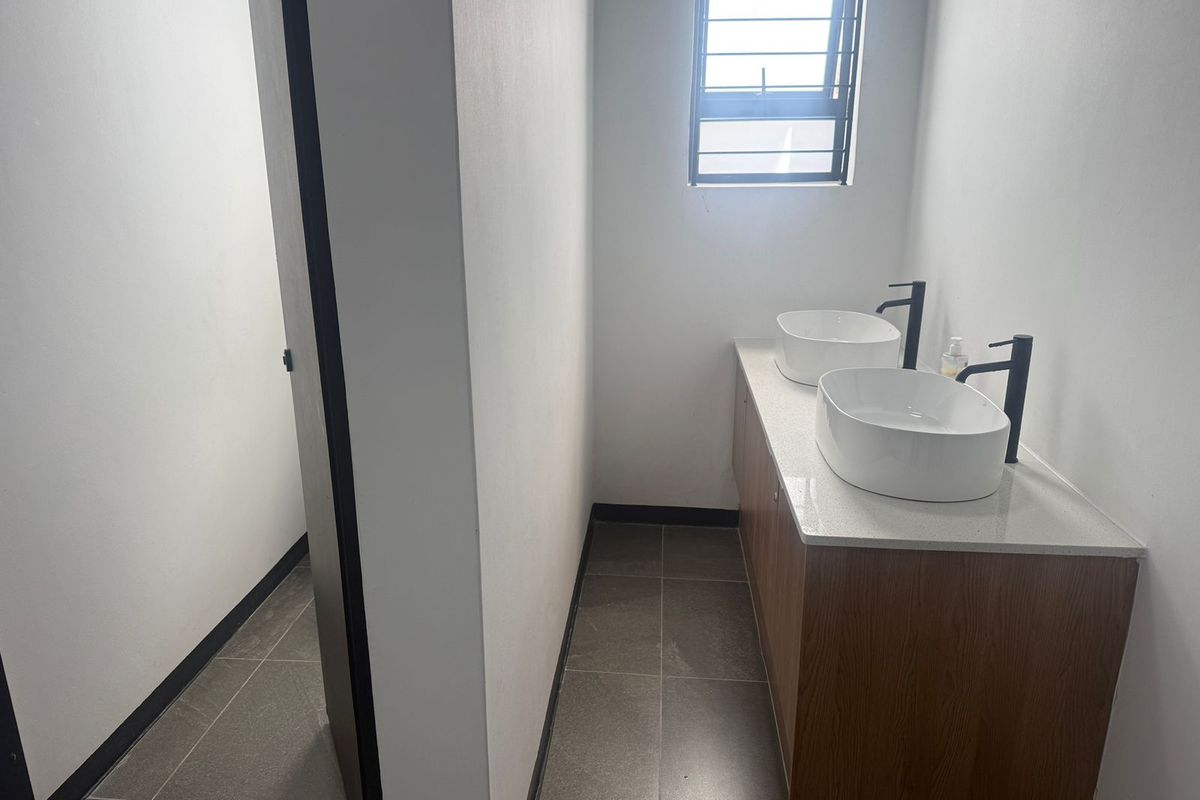 Modern bathroom featuring a double vanity with white vessel sinks, matte black faucets, and stone countertop, complemented by tiled flooring and a security-barred window.