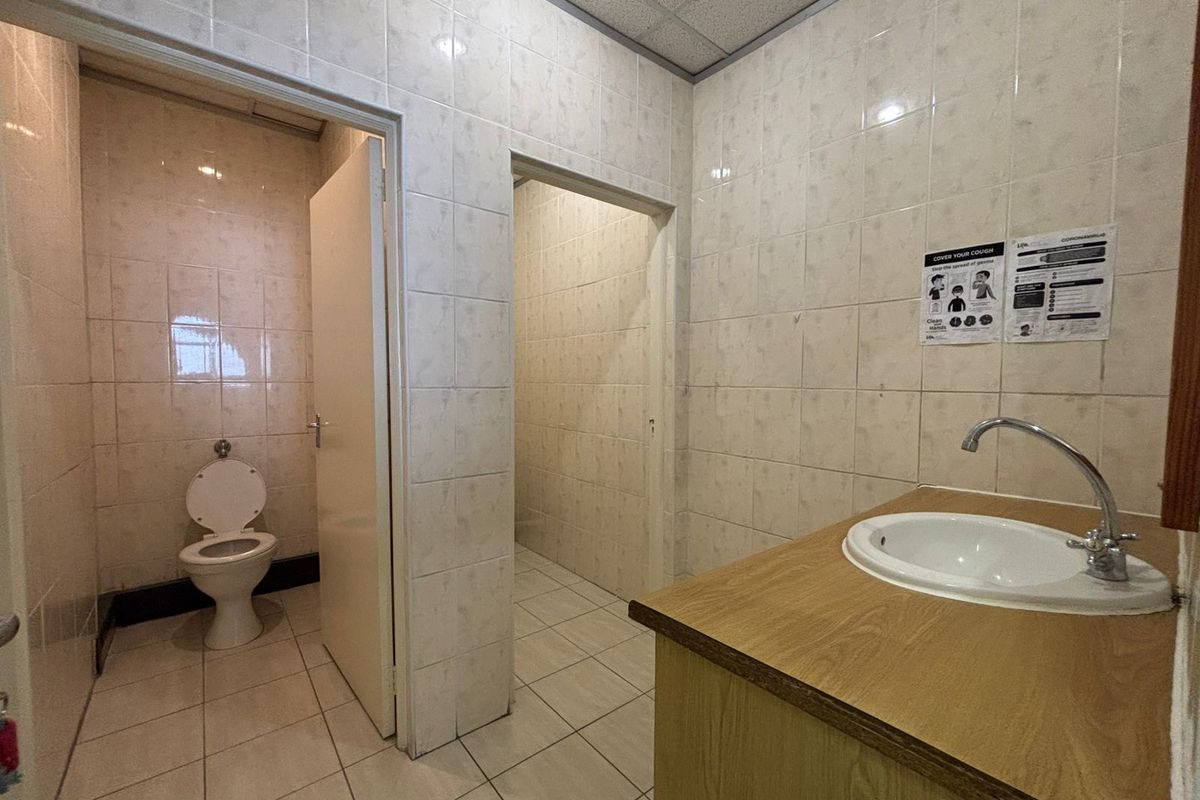 A functional commercial restroom facility featuring tiled walls, a built-in vanity with a basin, and a separate toilet cubicle.