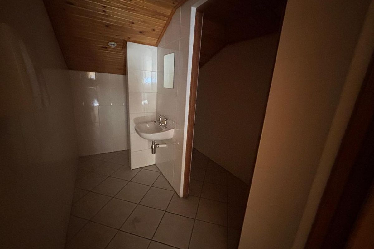 A functional bathroom space featuring tiled walls, a wall-mounted basin, and a sloped timber-paneled ceiling.