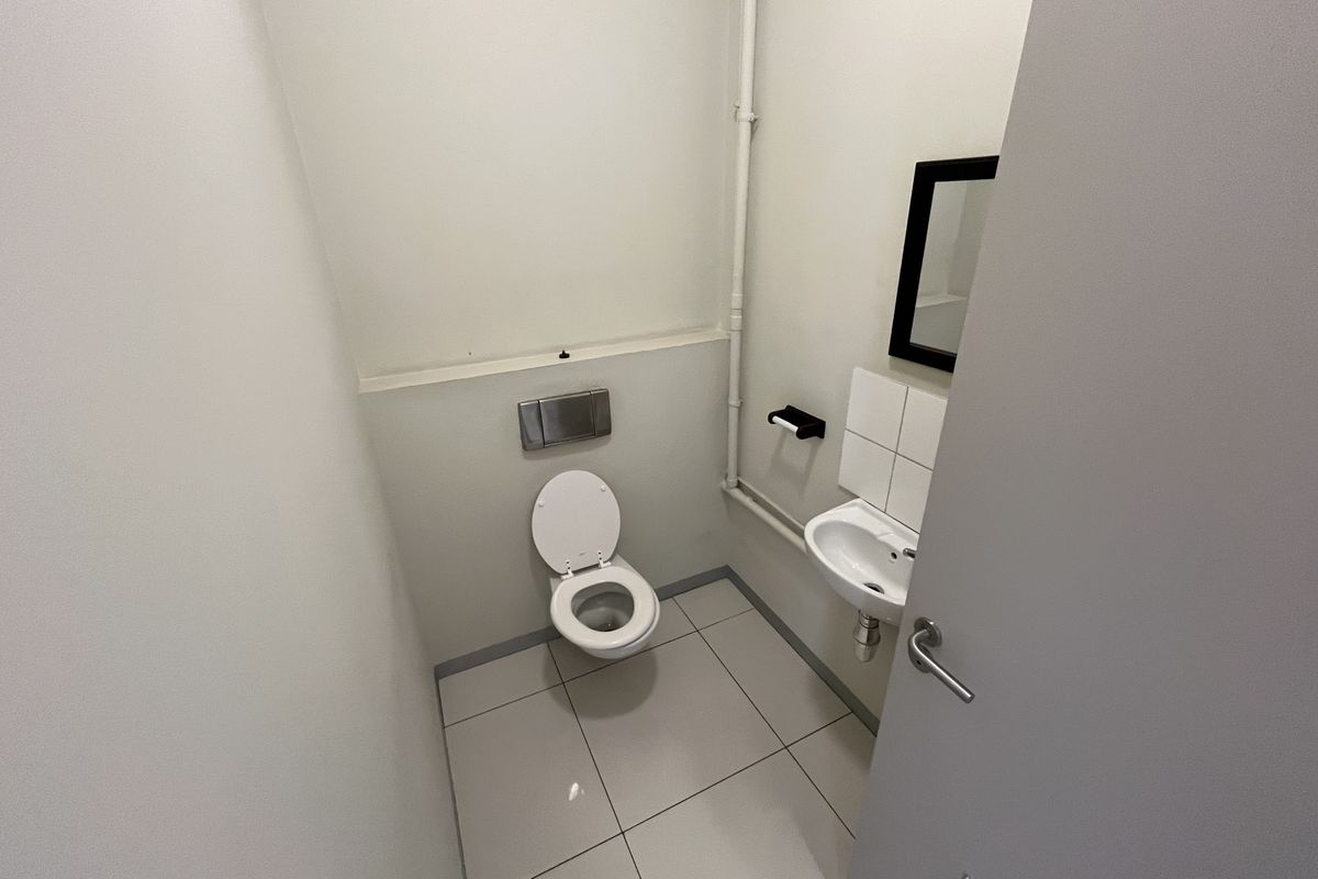 A compact, functional restroom featuring a wall-mounted toilet, a small basin with tiled splashback, and neutral floor tiling.
