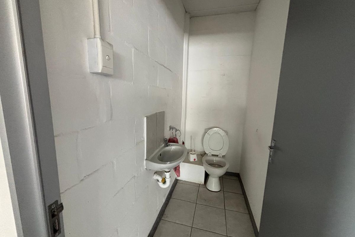 A functional industrial-style restroom featuring a wall-mounted basin and toilet with exposed brickwork and tiled flooring.