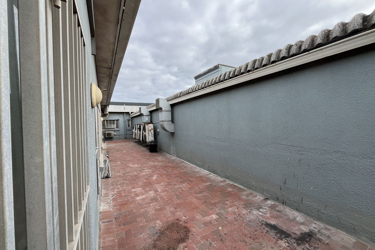 A narrow exterior side passage featuring red brick paving, perimeter walling, and mounted HVAC condenser units.
