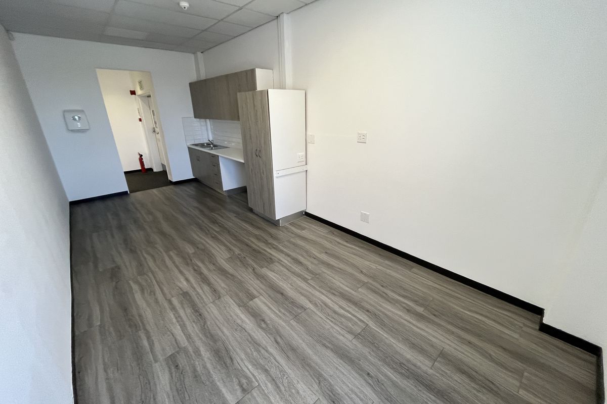 A clean, modern office kitchenette featuring wood-look vinyl flooring, built-in cabinetry, and a stainless steel sink.