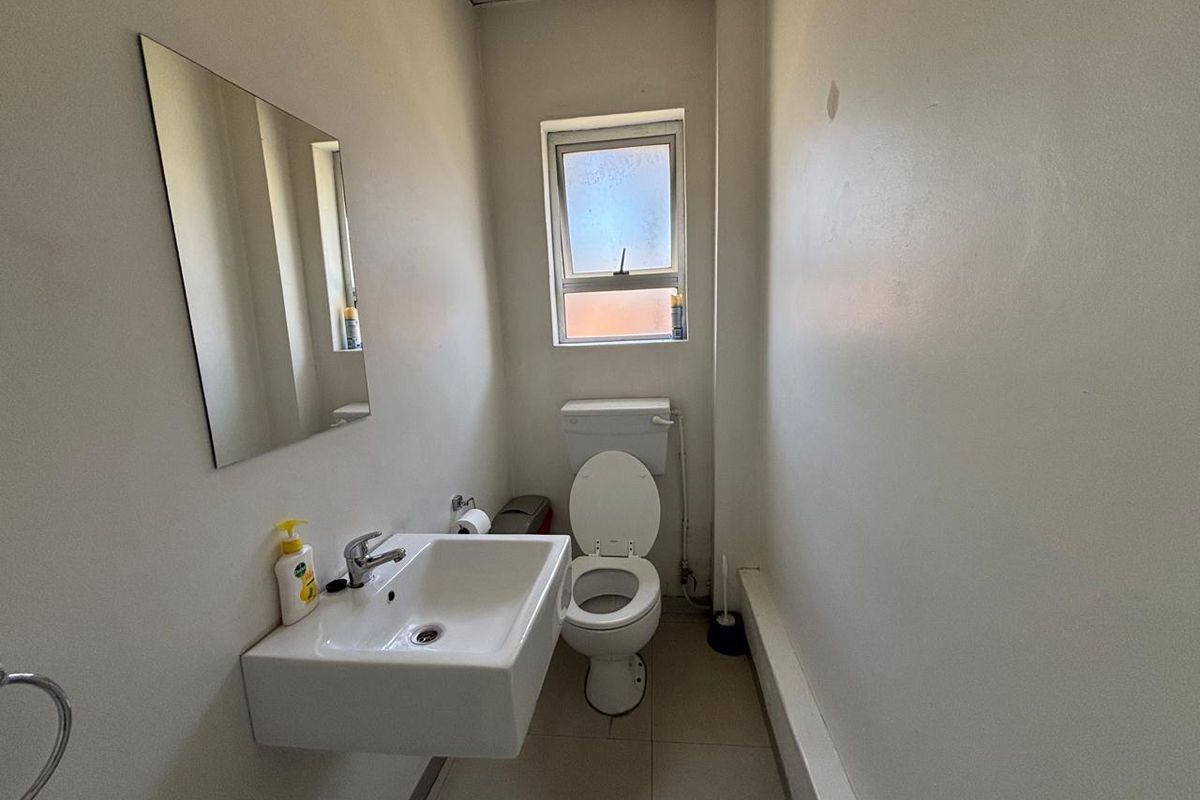 A functional industrial restroom featuring a wall-mounted basin, a standard toilet, and a small frosted window for natural light.