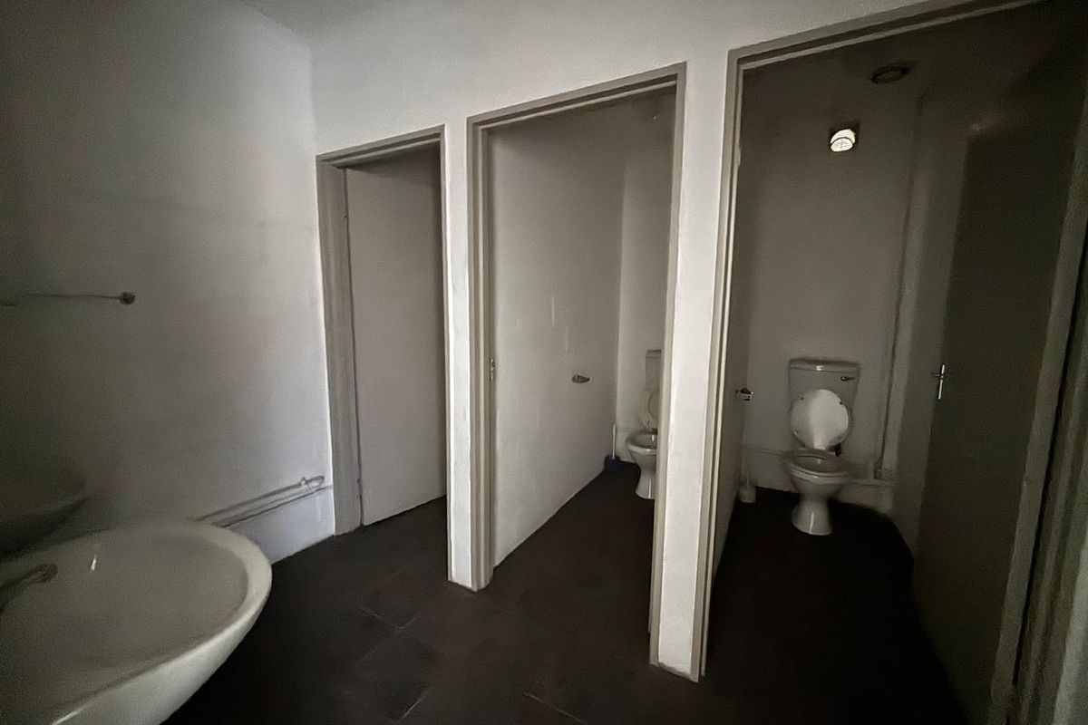 A functional office restroom facility featuring multiple toilet cubicles and a washbasin area with tiled flooring.