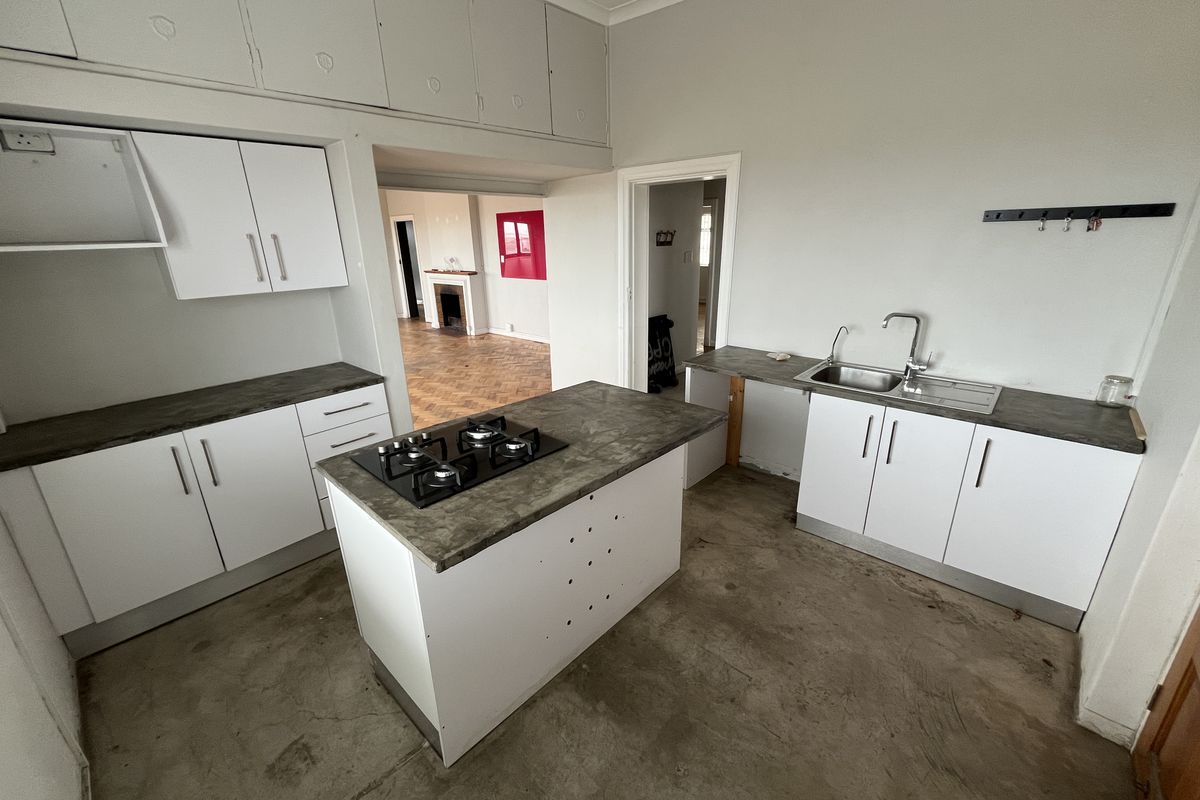 A functional kitchen area featuring white cabinetry, a central island with a built-in gas hob, and a stainless steel sink with a modern faucet.