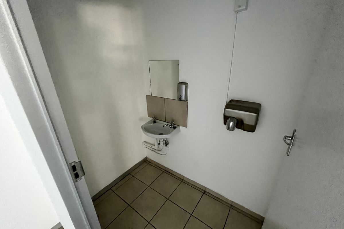 A functional restroom facility featuring a wall-mounted basin, mirror, and hand dryer with tiled flooring.